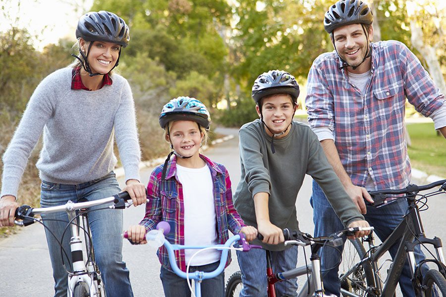 Employee Benefits - A Happy Family and Their Two Children are Together on Their Bikes at a Park on a Sunny Day