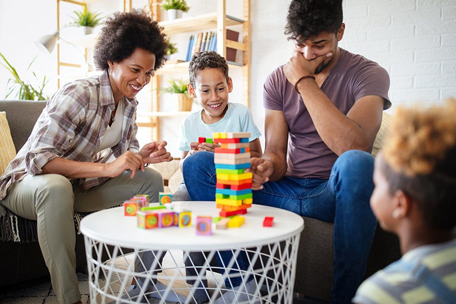 Personal Insurance - A Family and Their Two Children are Having Fun Sitting Together Around a Small Table Playing Jenga at Home