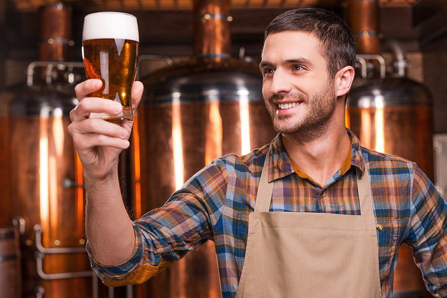 Specialized Business Insurance - A Brewer Wearing a Smok is Happily Looking at a Glass of Beer at His Brewery